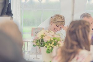 Bride wearing a veil laughing warmly at her wedding breakfast table during the speeches.